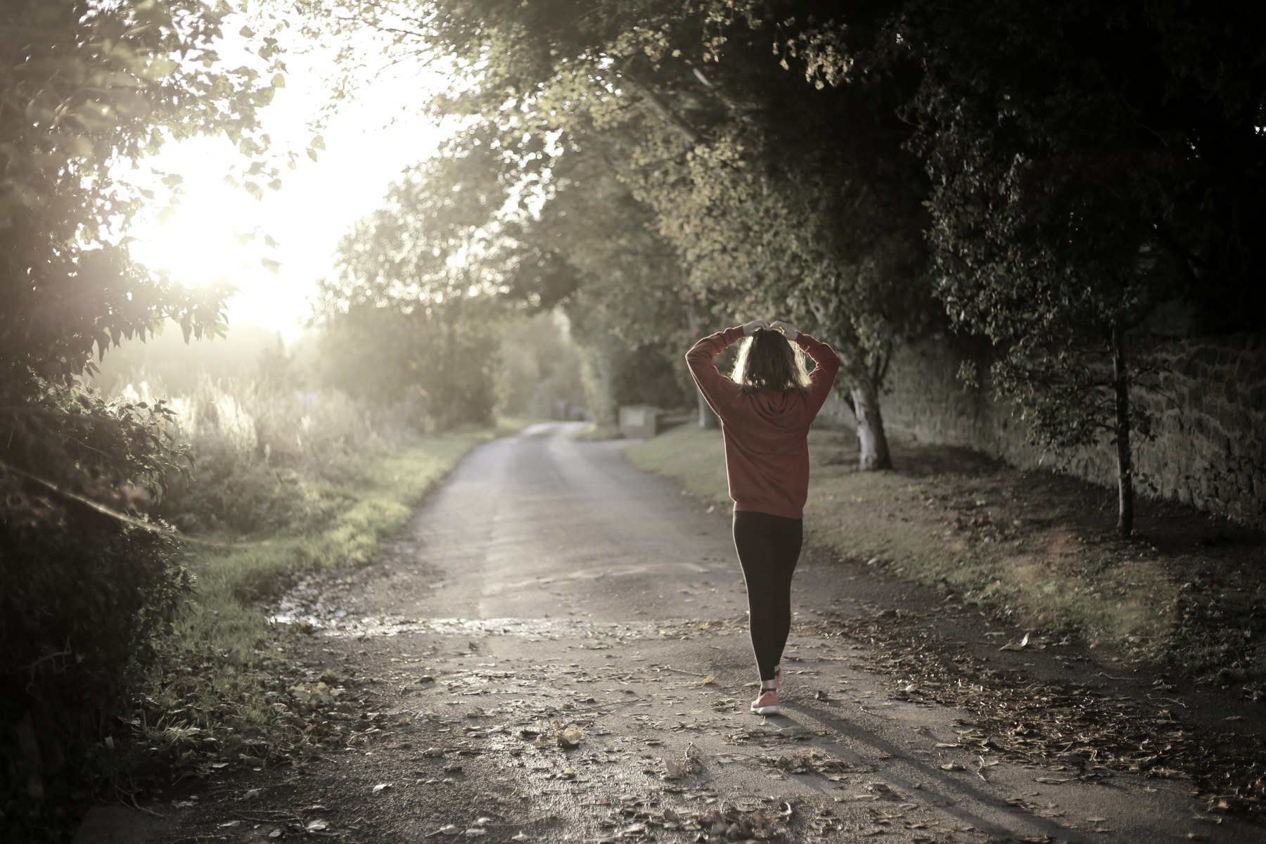 A woman walking on a tree-lined lane at sunrise